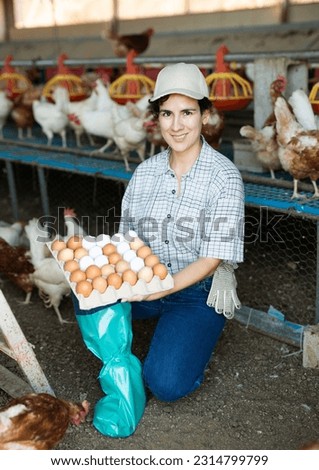 Positive young female farmer working in henhouse, collecting eggs