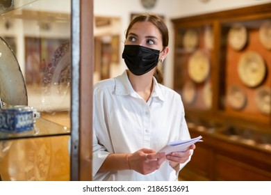 Positive Young Female In Protective Mask With Paper Guide Exploring Sculpture Art Pieces In Gallery