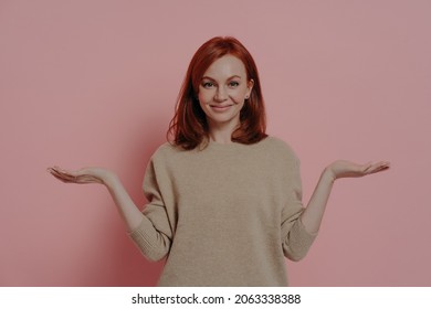 Positive Young Ginger Female Comparing Two Variants Options, Making Choice And Smiling At Camera, Standing Isolated On Pink Studio Background, Friendly Red-haired Woman Holding Two Objects On Palms