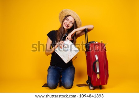 positive young girl in a hat rides in a long-awaited vacation with a large red suitcase, holds plane tickets
