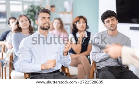 Positive young guy commenting something during a classroom training session in group