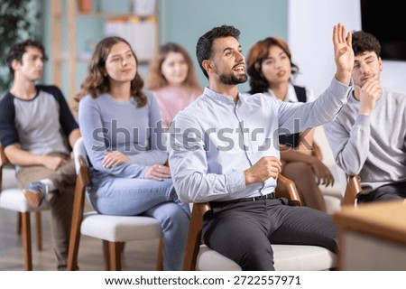 Positive young guy commenting something during a classroom training session in group