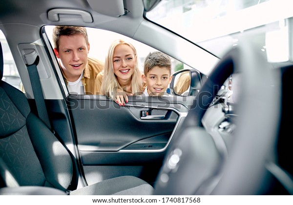positive young\
happy family inspecting car from inside, look at wheel and they are\
surprised with design of\
auto