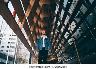 Positive young hipster guy dressed in stylish denim outfit exploring city urban setting feeling good on leisure, handsome Caucasian man in jeans jacket walking on street and smiling outdoors