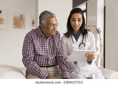 Positive young Indian doctor woman showing electronic content on tablet computer to senior Indian man, speaking to patient, explaining healthcare examination results - Powered by Shutterstock