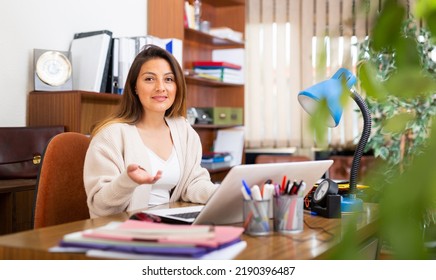 Positive Young Latin American Business Woman Sitting At Desk In Modern Office Interior, Working With Laptop.