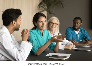 Positive young Latin surgeon woman speaking at professional meeting to multiethnic colleagues, offering ideas for collaboration, brainstorming. Diverse practitioners discussing doctor occupation - Powered by Shutterstock