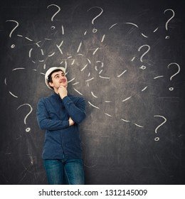 Positive young man engineer wearing protective helmet holding hand under chin looking up thoughtfully in front of a blackboard try to solve different tasks, having questions. - Powered by Shutterstock