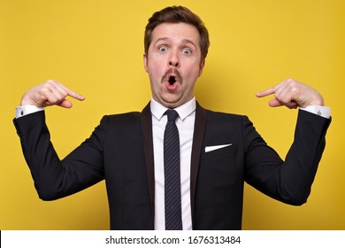 Positive young man with mustache smiling and pointing at himself with index fingers. Handsome man wearing suit gesturing and looking at camera. Self presentation concept. - Shutterstock ID 1676313484