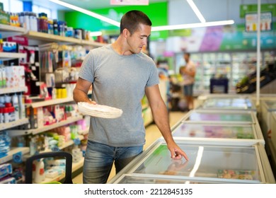 Positive Young Man Shopping In Supermarket, Choosing Frozen Convenience Food For Quick Dinner...