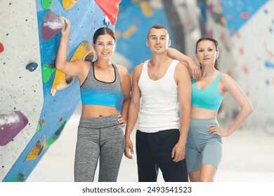 Positive young man and two women posing together at artificial rock wall in climbing hangar - Powered by Shutterstock