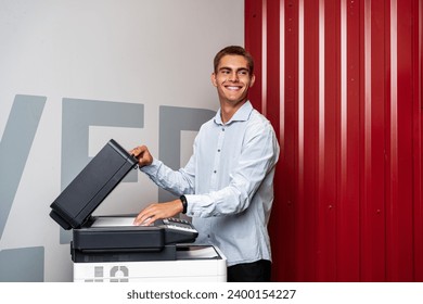 Positive young man using printer in the modern office