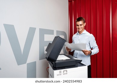 Positive young man using printer in the modern office