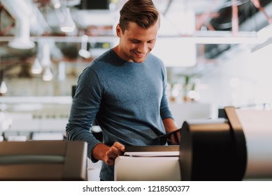 Positive Young Man Working In The Office While Using A Printer With Pleasure