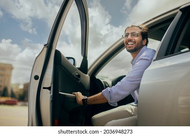 Positive young middle-eastern man going out the car, low angle photo, copy space. Happy arab guy open automobile door and smiling, getting in. Auto test-drive, leasing, buying, renting concept