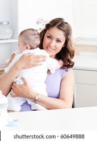 Positive Young Mother Holding Her Baby In The Kitchen At Home