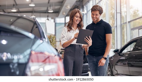 Positive junge professionelle Vertriebsmitarbeiterin, die männlichen Kunden ein Dokument vorführt, das sie beim Kauf eines neuen Autos in Händen
