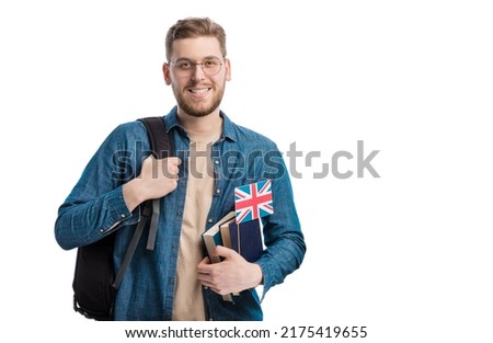 Positive young student with books, backpack and UK flag standing over white studio background. Happy man studying at english university on exchange program.