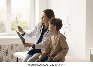 Positive young traumatologist in medical coat holds roentgen film show to little patient, explain fracture, review successful recovery treatment result after trauma at visit in clinic office. Medicine - Powered by Shutterstock