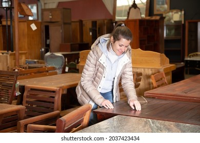 Positive young woman choosing dining table while visiting furniture salon 