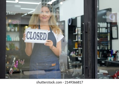 Positive young woman closing hair salon in the evening, she is standing at entrance with sign in hands - Powered by Shutterstock