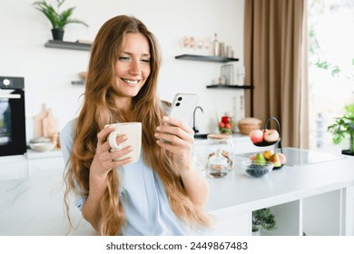 Positive young woman having breakfast while scrolling social media on cellphone at home kitchen. Caucasian female girl using smart phone for social media, remote work, online shopping - Powered by Shutterstock