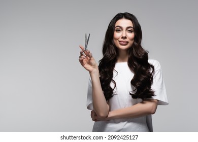 Positive Young Woman With Long Wavy Hair Holding Scissors Isolated On Grey