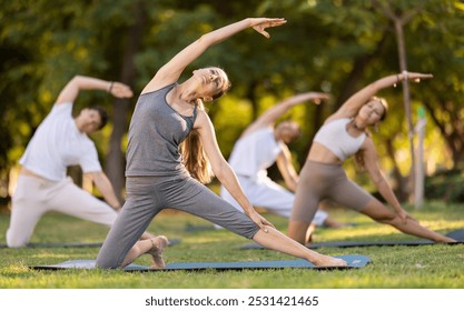 Positive young woman performing yoga asanas on mat on green glade in serene sunlit summer park, enjoying group session and relaxation in nature. Healthy sports lifestyle concept.. - Powered by Shutterstock