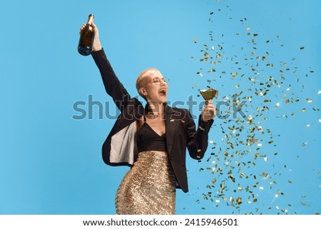 Positive young woman raising hands up of happy and joy and drinking sparkling wine against blue studio background. Concept of Friday mood, celebration, holidays and parties, human emotions.
