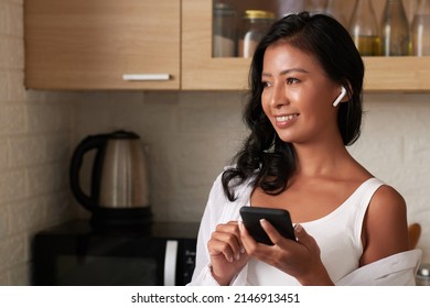 Positive young woman wearing earbuds when making call to friend or colleague