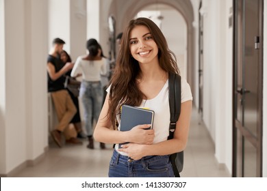 Positivity beautiful girl smiling at camera, standing on corridor with notes as backpack, going to lesson. Happy brunette female student studying in luxury university. - Powered by Shutterstock