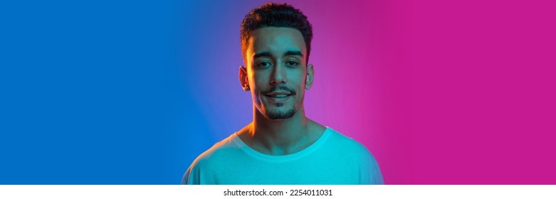 Positivity  Young man in casual white T  shirt posing  looking at camera over gradient blue pink background in neon light  Banner  flyer  Concept emotions  facial expression  sales  ad  fashion