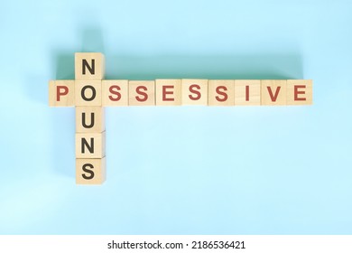Possessive nouns concept in English grammar education. Wooden block crossword puzzle flat lay in blue background. - Shutterstock ID 2186536421