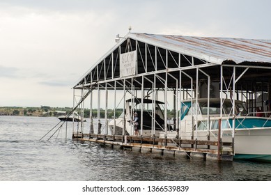 Possum Kingdom Lake, Texas / USA June 21 2017 A Young Boy Wearing A Hoodie And Life Jacket Fishes Off Of A Dock In The Marina With A No Wake Sign Overhead And A Boat In The Background