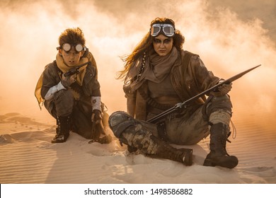 Post apocalyptic woman and boy with weapons outdoors. Desert in smoke and dead wasteland on the background. Aggressive girl warrior in shabby clothes holding sword and young boy with gun and chain