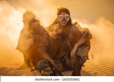 Post apocalyptic woman and boy with weapons outdoors. Desert in smoke and dead wasteland on the background. Aggressive girl warrior in shabby clothes holding sword and young boy with gun and chain