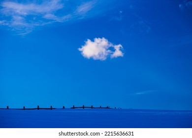 Post Fence Underneath Clouds Over A Blue Barren Snowy Winter Landscape In The New England Town Of Stowe Vermont, USA