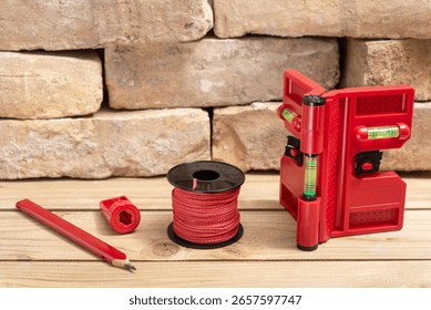 Post leveler for the vertical and horizontal alignment of posts with plumb line, carpenters pencil and sharpener for pencil next to old bricks on wooden table.