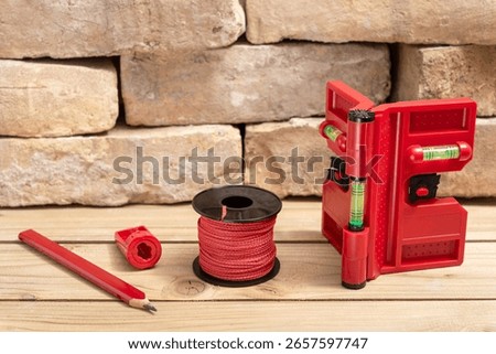 Post leveler for the vertical and horizontal alignment of posts with plumb line, carpenters pencil and sharpener for pencil next to old bricks on wooden table.