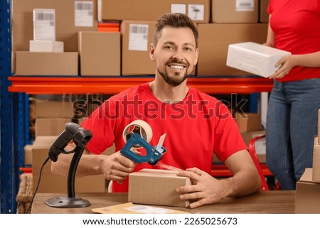 Post office worker packing parcel at counter indoors