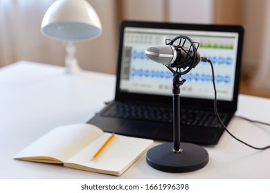 Post Production And Technology Concept - Microphone, Laptop Computer With Sound Editor Program, Headphones And Notebook On Table At Home Office