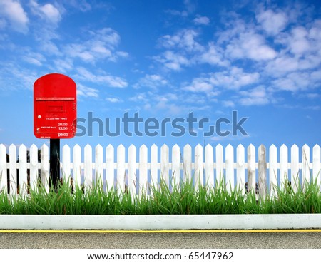 postbox on road side with white fence and blue sky