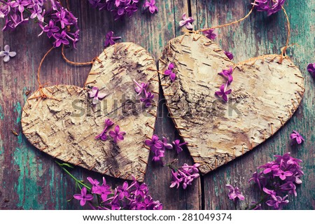 Postcard with two decorative hearts and fresh lilac flowers on green aged wooden background. Selective focus. Toned image.