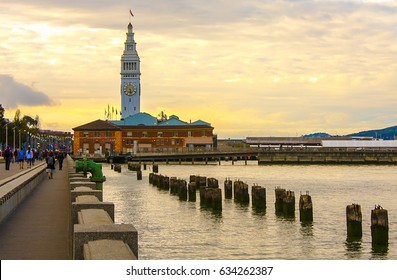 Postcard-like image of the boardwalk/embarcadero leading to the Ferry Building in San Francisco. The sky is highlighted with gorgeous yellow pre-sunset cloud covering.