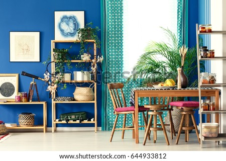 Postcolonial room with wooden bookcase, dining table, chairs, pattern curtain