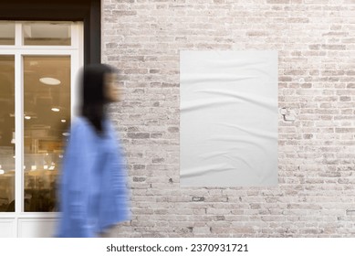 Poster adhered to a brick wall next to a shop door. Woman in motion walking beside. The urban scene with dynamic movement for poster mockup and design promotion