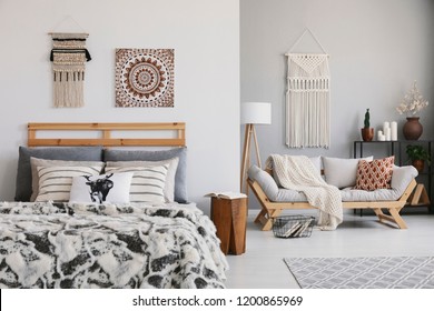 Poster And Decor Above Patterned Bed In Hygge Flat Interior With Pillows On Wooden Sofa. Real Photo