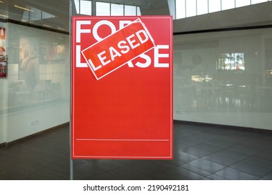 Poster Of 'For Lease' With A 'Leased' Sign On Top In Front Of A Vacant Shop. Concept Of Rental Commercial Property Or Retail Space. Background Texture With Copy Space For Your Own Text. 