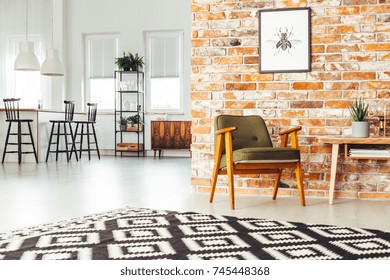 Poster On Red Brick Wall Above Green Retro Chair Next To Wooden Table In Spacious Living Room With Geometric Carpet