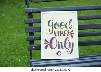 Poster with phrase Good Vibes Only on black wooden bench outdoors
